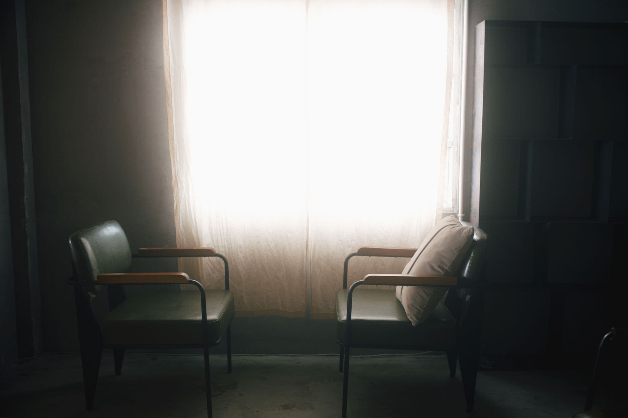 Two chairs facing a curtained window in soft afternoon light